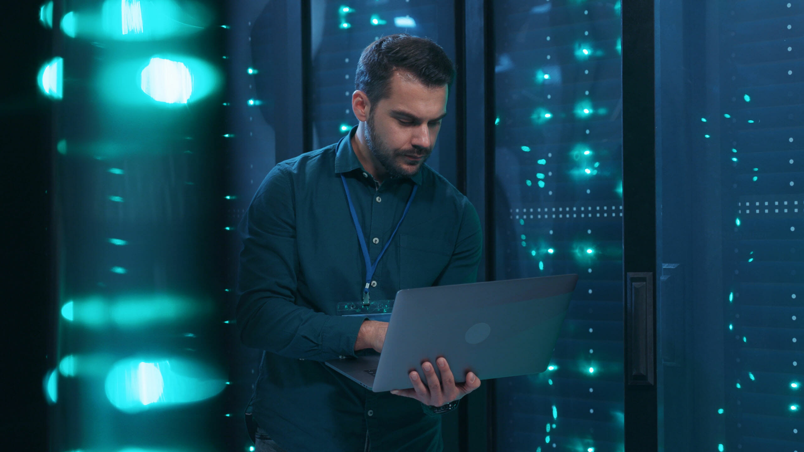 IT professional admin using laptop computer doing data transfer operation with rack server cabinets in digital room of data center.